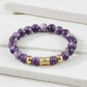 Macro shot of purple amethyst beads with hexagonal gold accents on a white stone background