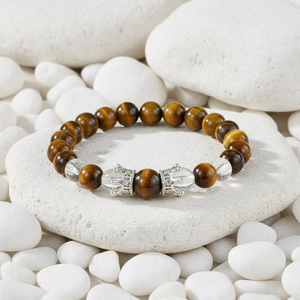 Detail of tiger eye beads with silver crown charms on white pebbles background
