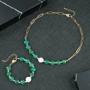 Detail von verstellbarer goldener Gliederkette und grünem Perlenarmband auf Marmor