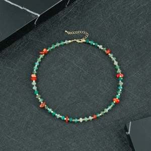 Detail van kralenketting met groene facetkralen, rode stenen en gouden karabijnsluiting