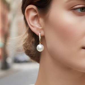 Gros plan d'élégantes boucles d'oreilles perles dorées avec zircons brillants sur un modèle