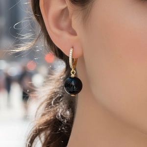 Gros plan de boucles d'oreilles dorées avec zircons et perles d'agate noire suspendues