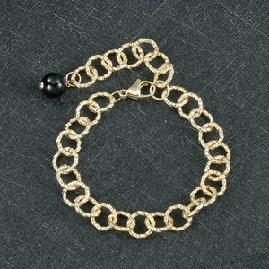 Vue détaillée d'un bracelet doré à maillons texturés avec une perle noire élégante