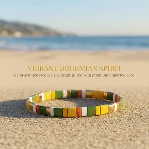 Bracciale bohémien con perline Tila colorate su sfondo di spiaggia sabbiosa tropicale