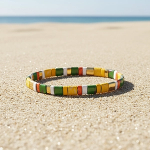 Bracciale elastico con perline Tila colorate e smalto su sfondo di sabbia bianca