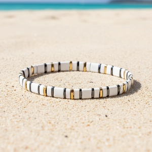 Dettaglio del bracciale Tila sulla sabbia con perline bianche, dorate e grigie