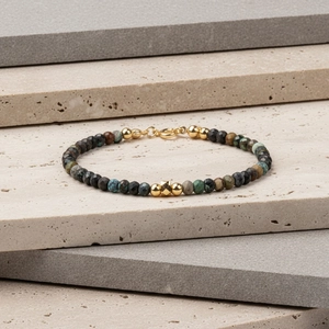 Armband van gefacetteerde natuursteen met gouden kralen op een stenen standaard
