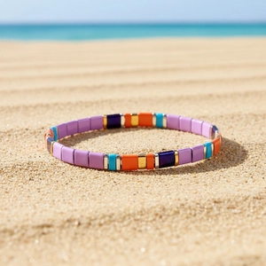 Primo piano del braccialetto elastico con piastrelle colorate boho su sfondo di sabbia