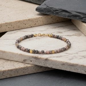 Macro detail van roze natuursteen kralenarmband met gouden kubussen en karabijnsluiting