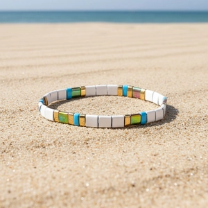Bracciale boho con perline Tila smaltate colorate posizionato su sabbia dorata al mare