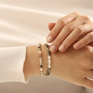 Detailopname van gelaagde zoetwaterparel armbanden met halfedelstenen en gouden accenten