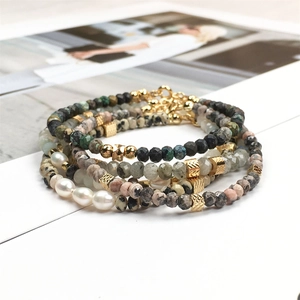 Detailopname van meerlagige armband met natuurstenen, parels en vergulde metalen accenten