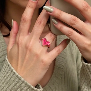 Gros plan d'une bague coeur en émail rouge sur la main avec fond en tricot vert