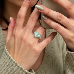 Bague cœur multi-couches en émail vert et finition dorée sur l'index d'une femme