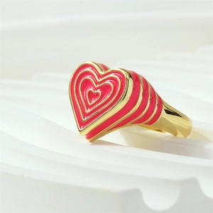 Gros plan d'une bague coeur en émail rose avec anneau doré et design multicouche