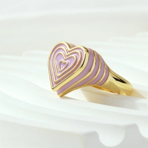Vue latérale macro d'une bague coeur dorée avec émail rose-violet sur support blanc