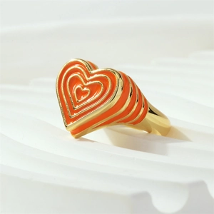 Gros plan d'une bague chevalière dorée avec un design de cœur en émail orange multicouche