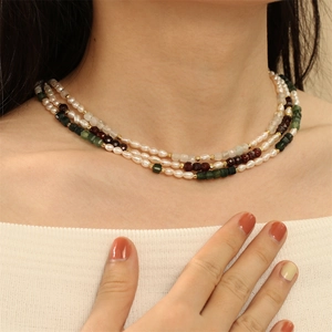 Detail of multi-layer necklace with freshwater pearls and green gemstones on neck