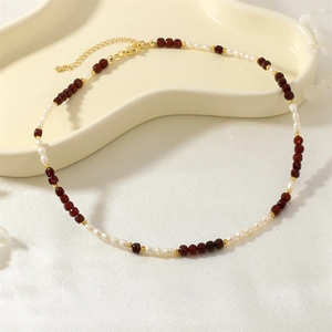 Detailed view of red faceted beads and irregular white pearls on a gold chain necklace