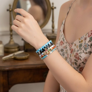 Detail of stacked bohemian beaded bracelets featuring a rainbow evil eye charm on wrist