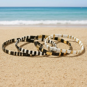 Three-piece bohemian Tila bead bracelets set in black, white and gold on beach sand