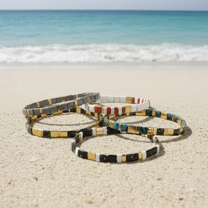 Five bohemian Tila bead bracelets on white sand beach with blue ocean backdrop