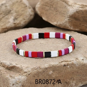 Detail view of colorful enamel bead bracelet with gold metal spacers on natural stone background