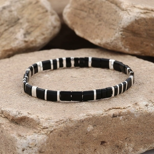 Detail view of black matte tile bracelet with silver spacers on natural rock surface
