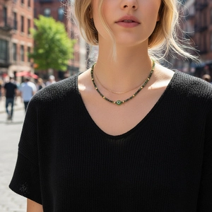 Detail of layered green beaded necklace and gold chain with evil eye charm on model