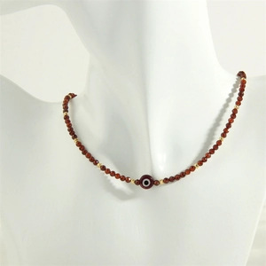 Detail view of handmade garnet beaded necklace with a red evil eye charm and gold spacers