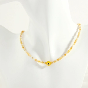 Detail of beaded evil eye necklace with yellow semi-precious stones on white mannequin