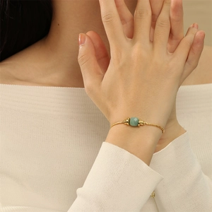 Detail eines 18K vergoldeten verstellbaren Armbands mit grünem Edelstein am Handgelenk