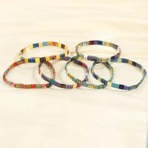 Detail of stacked colorful enamel Tila bead bracelets on soft satin fabric background