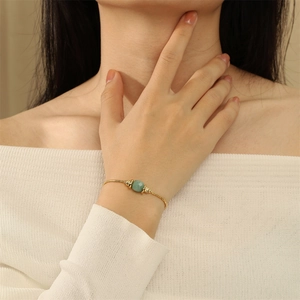 Detail eines 18K vergoldeten Armbands mit grünem Edelstein am Handgelenk eines Models