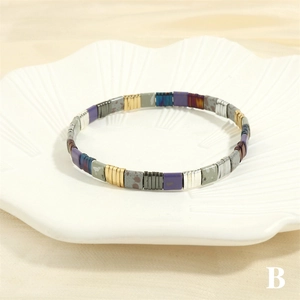 Close-up of Tila bead bracelet with purple and gold enamel tiles on a shell tray