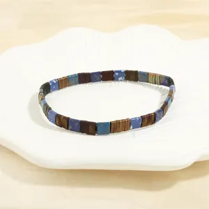 Detailed shot of multi-color Tila beads elastic bracelet on a white textured ceramic dish