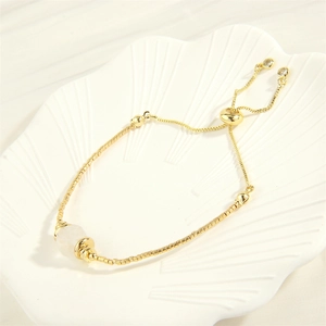 Detail eines verstellbaren 18K Goldperlenarmbands mit weißem Naturstein auf einer Muschel