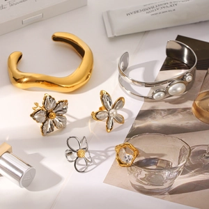 Flat lay of gold and silver irregular bracelets and floral rings on artistic background