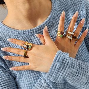 Close-up of stacked gold-plated stainless steel rings with natural stones on blue sweater