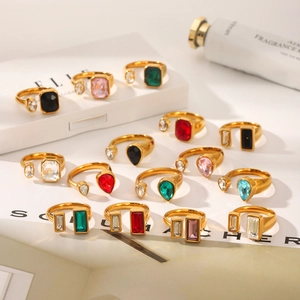 Anelli aperti dorati con zirconi geometrici colorati su una confezione regalo