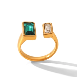 Dettaglio dell'anello dorato aperto con pietre rettangolari verde smeraldo e bianche
