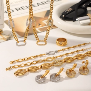 Detalle de set de joyas de cadena cubana bicolor con cristales en superficie blanca