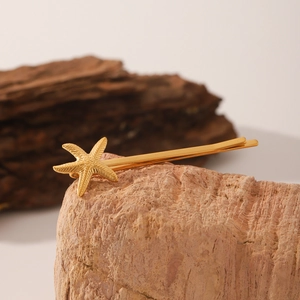 Macro d'une pince à cheveux étoile de mer dorée 18K sur pierre et écorce rustique