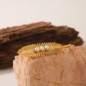 Close-up of golden leaf hair clip featuring three elegant white pearls on a stone surface