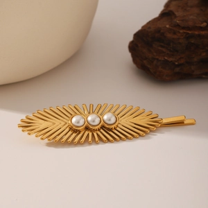 Elegant gold leaf hairpin with three white pearls on a minimalist textured background