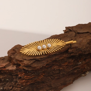 Macro shot of leaf-shaped golden hair clip with three pearls on rustic wood texture