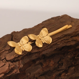Elegant gold butterfly hair clips featuring detailed metallic wings on a rustic bark background