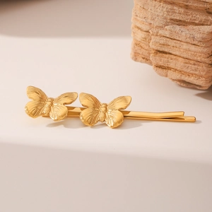 Elegant gold butterfly hair clips with textured metal wings displayed on a stone surface