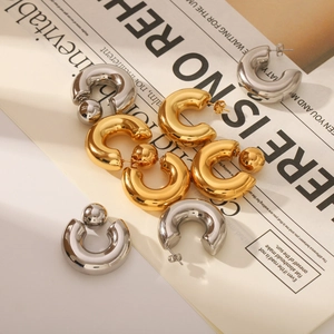 Chunky C-shaped hoop earrings in gold and silver finish on a vintage newspaper background
