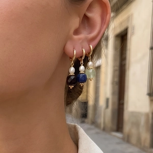 Primo piano di orecchini d'oro con perle e pietre preziose naturali indossati da modella